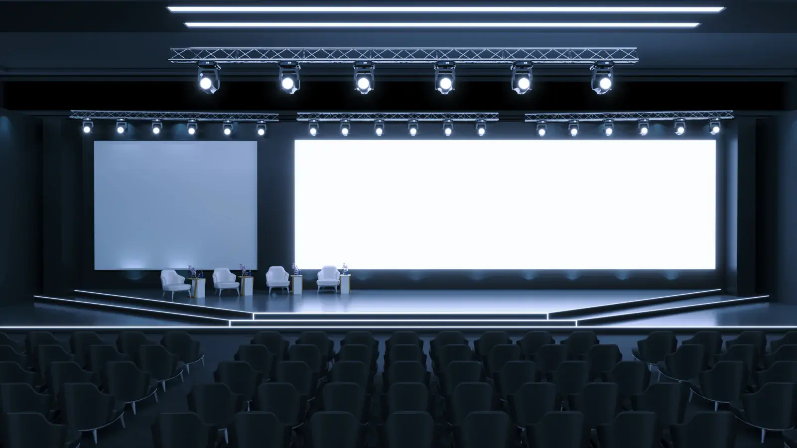 Conference stage with a wide bright screen and lounge chairs, with rows of seats in front