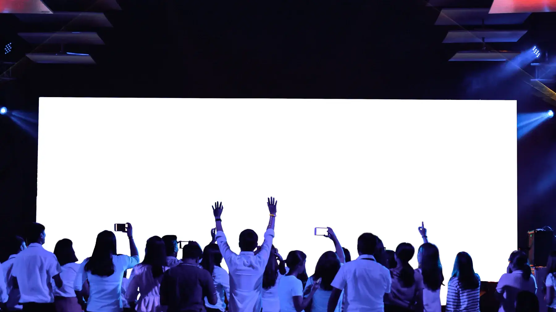 Cheering crowd silhouetted in front of a huge bright screen